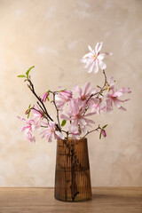 Magnolia tree branches with beautiful flowers in glass vase on wooden table against beige background © New Africa
