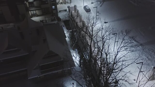 People walking on snowy streets of Zakopane city at night, Poland. Aerial forward top-down reveal