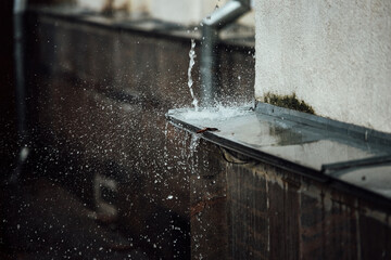 falling raindrops break on the ledge. splashes from running water. drainpipe from the roof of a building during a rainstorm