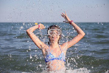 young caucasian girl plays in the sea water making splashes and jumps