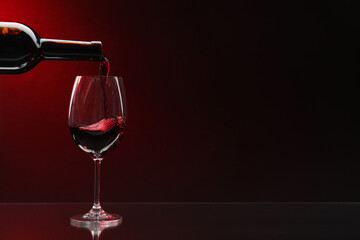 Pouring red wine from bottle into glass on dark background, space for text - obrazy, fototapety, plakaty