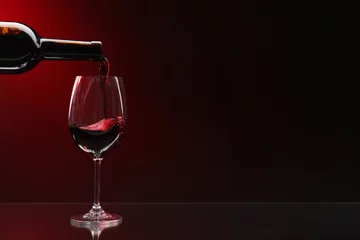 Fotobehang Pouring red wine from bottle into glass on dark background, space for text © New Africa