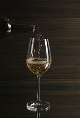 Pouring white wine from bottle into glass on table against wooden background