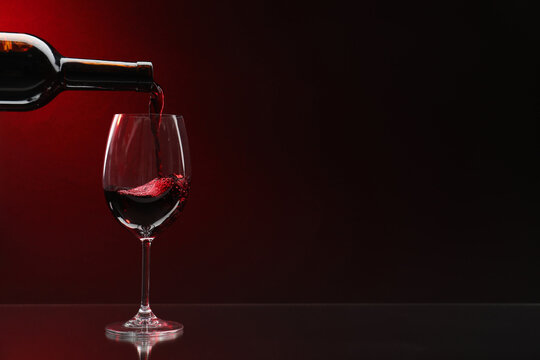 Pouring red wine from bottle into glass on dark background, space for text