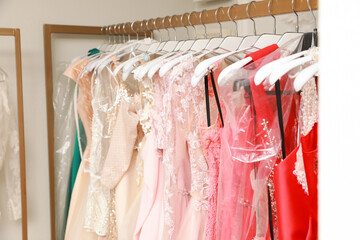 Different beautiful dresses on hangers in rental clothing salon