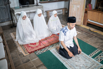 asian muslim family praying jamaah together at home. sholat or salah wearing white and hijab