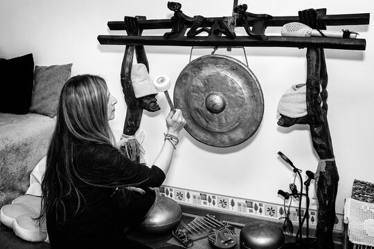 Adult Woman Playing Gong- Music Therapy. Portrait Of A Happy Woman Striking A Gong For Meditation.