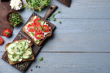 Delicious sandwiches with vegetables, cheese and microgreens on grey wooden table, flat lay. Space for text