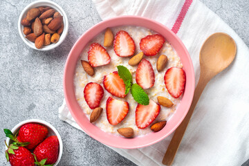 oatmeal porridge with strawberries, almonds, mint leaf in pink bowl, spoon and napkin with red stripes on concrete background Top view Flat lay Vegan food concept Healthy breakfast
