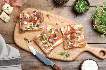 Delicious sandwiches with prosciutto, cheese and microgreens on wooden table, flat lay