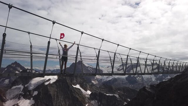 Woman with a Swiss flag on highest suspension bridge in Europe: Titlis bridge crossing the peak on top of Titlis glacier in the Uri Alps. Canton of Obwalden at 3028 meters. Switzerland in summer.