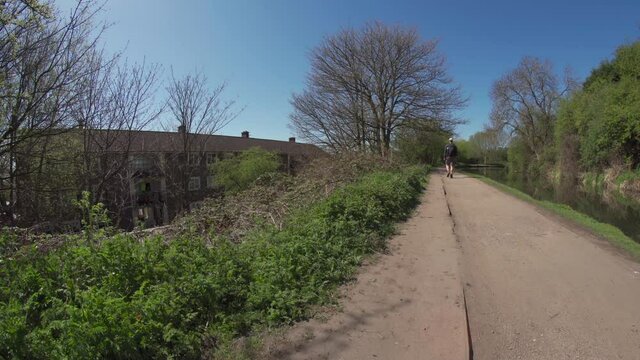 A man walking a UK canal with council flat housing estate on the left