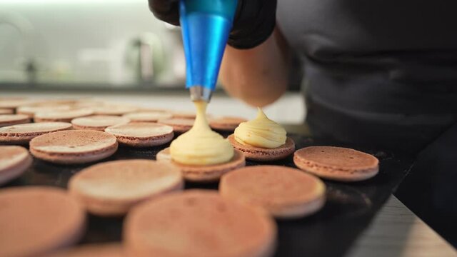 Process Of Making macaroon at home. Shot of hands of female pastry chef holding white macaron with ganache and squeezing red fruit jam from bag. Nature pastry macaroons. High quality 4k footage