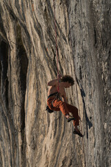 Male climber sweeps holds on the rock with a brush while held by a rope.