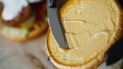Chef in black gloves smears a bun with mustard for hamburger.
