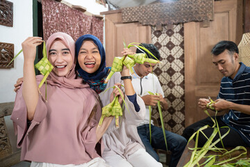 Obraz na płótnie Canvas excited asian muslim woman making ketupat rice with coconut leaf during ramadan kareem preparing for eid fitri mubarak celebration