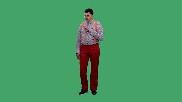 Bored man showing blah blah blah gesture. He listens to lies, nonsense, empty promises. Portrait of a man in glasses, a plaid shirt with orange suspenders in the studio on a green screen. Slow motion.