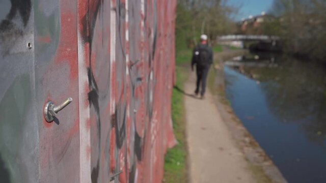 A man walking a canal past old industrial steel and bent bolts