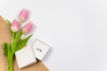 Obraz premium Pink tulips with ring as a gift on white background with crafting paper. Mother's Day, Valentine's Day, Easter. Copy space Flat lay