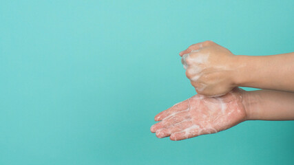Hands washing gesture with foaming hand soap on mint green and Tiffany Blue background.