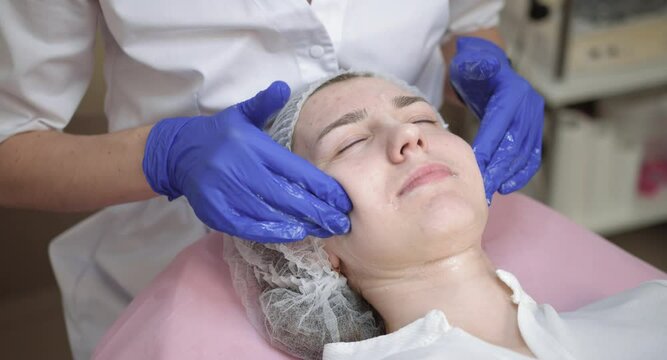 Young woman in medical hat, lying on a medical couch at cosmetology office. Young lady doctor in medical mask and gloves, cleaning her forehead. Hydration and rejuvenation of the skin