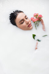 young woman relaxing in milk bath with pink roses.