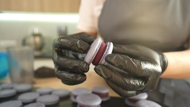 Process Of Making macaroon at home. Shot of hands of female pastry chef holding white macaron with ganache and squeezing red fruit jam from bag. Nature pastry macaroons. High quality 4k footage