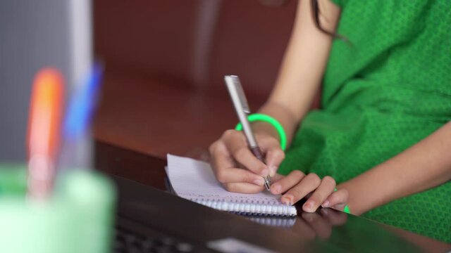 Close up of unrecognizable Kid writing notes during online class from laptop - concept of new normal education, virtual learning due to coronavirus or covid-19 pandemic.