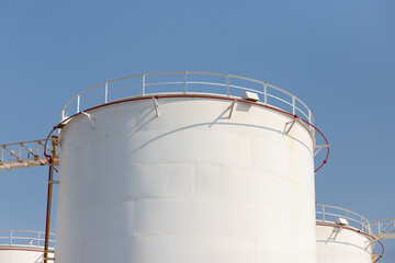 Obraz premium white petroleum steel tanks against blue sky, white metal silo with rust, liquid metal container.