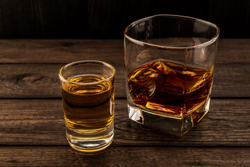 Glass of brandy and tequila on an old wooden table. Angle view, focus on the glass of tequila