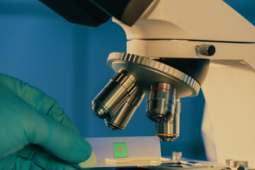 Glass slide with a tissue in hand and a scientific microscope. Screening biopsy sample in medical...