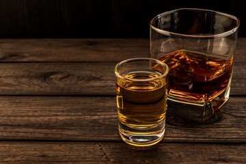Glass of brandy and tequila on an old wooden table. Angle view, focus on the glass of tequila