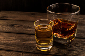 Glass of brandy and tequila on an old wooden table. Angle view, focus on the glass of tequila