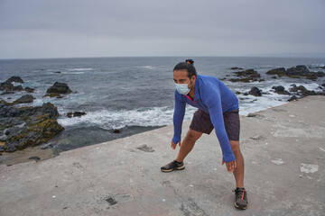 Man with mask performs stretching exercises in front of the sea. New normality. Sports