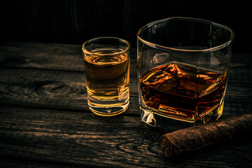 Glass of brandy and tequila with cuban cigar on an old wooden table. Angle view, focus on the cuban cigar