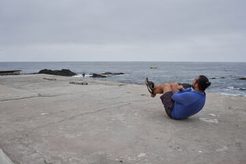 Man performs sit-ups in front of the sea. New normality. Sports - obrazy, fototapety, plakaty