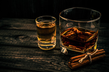 Glass of brandy and tequila with cinnamon sticks tied with jute rope on an old wooden table. Angle view, focus on the cinnamon sticks