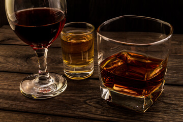 Three glasses with brandy, tequila and red wine on an old wooden table. Angle view