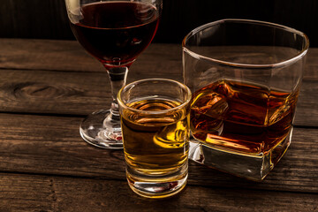 Three glasses with brandy, tequila and red wine on an old wooden table. Angle view