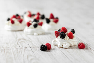 Pavlova's cake on a light wooden table. Cake with meringues, raspberries and blackberries. High quality photo