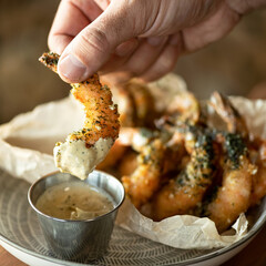 Male hand holds fried king prawn or shrimp dipping it in sauce. Seafood concept. Spicy oriental...