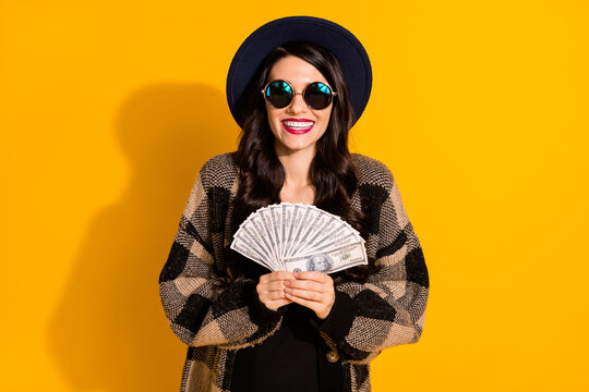 Photo of pretty brunette young woman hold money rich wear cool glasses isolated on yellow color background