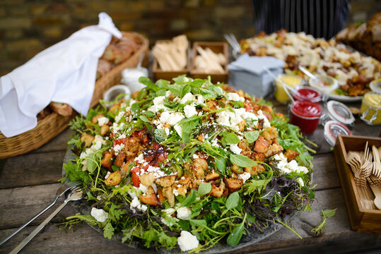 Fresh salad with rucola lettuce tomatoes cheese and other ingredients on wooden table. Rustic garden party concept.