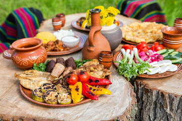 Homemade Romanian Food with grilled meat, polenta and vegetables Platter on camping. Romantic traditional Moldavian food outside on the wood table.