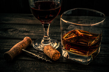 Glass of brandy and red wine with corkscrew and cork on an old wooden table. Angle view