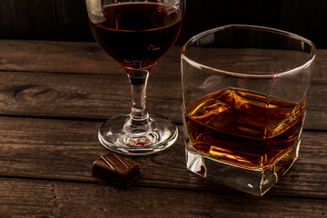 Glass of brandy and red wine with chocolate on an old wooden table. Angle view