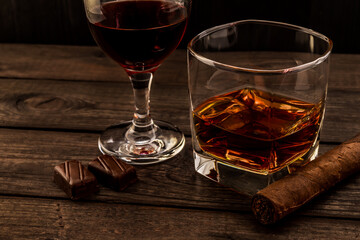Glass of brandy and red wine with chocolate and cuban cigar on an old wooden table. Angle view,...