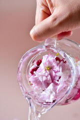 Water pours from a glass jug with pink flowers, on a pink background.