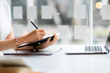 An Asian female is taking notes on her notebook for online classes, study ideas and note-taking.