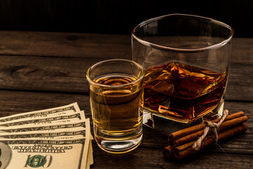 Glass of brandy and tequila with money and cinnamon sticks tied with jute rope on an old wooden table. Angle view